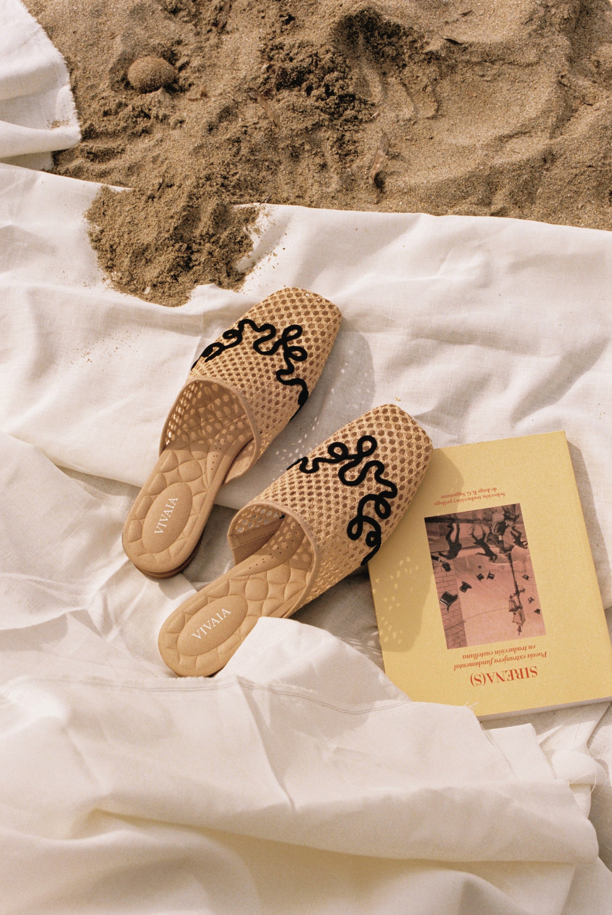 Flat sandals arranged on sand and white fabric inside a film-frame border