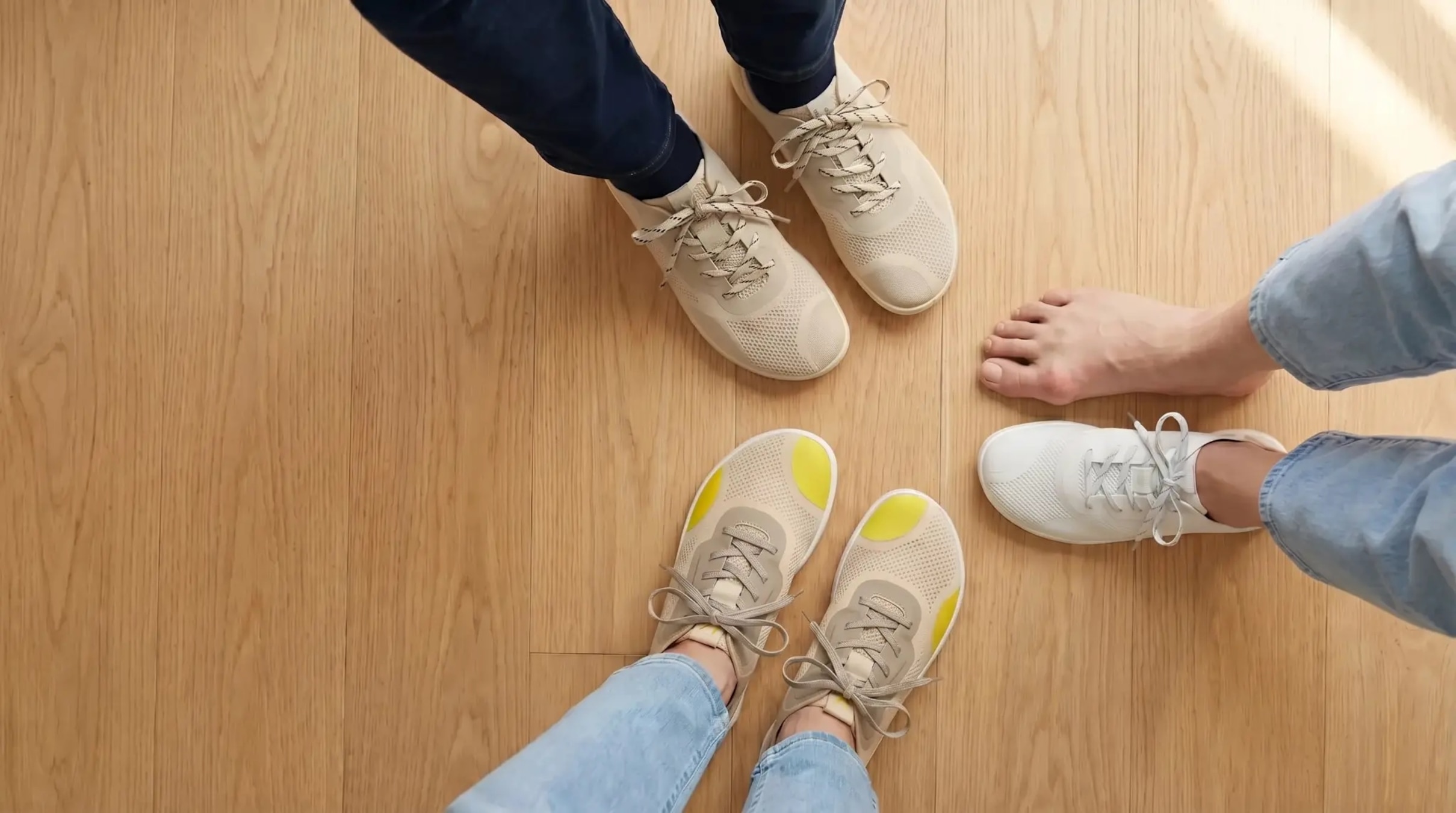 Top-down lifestyle banner showing Maven beside ordinary sneakers and a bare foot on a light wood floor