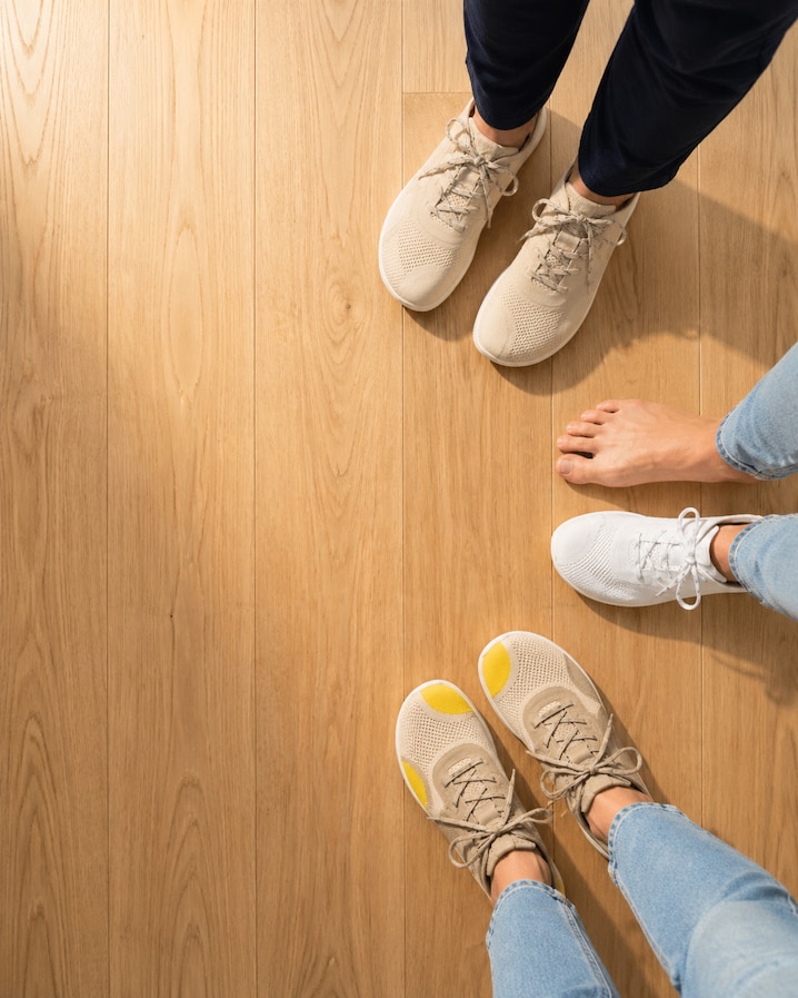 Top-down lifestyle banner showing Maven beside ordinary sneakers and a bare foot on a light wood floor