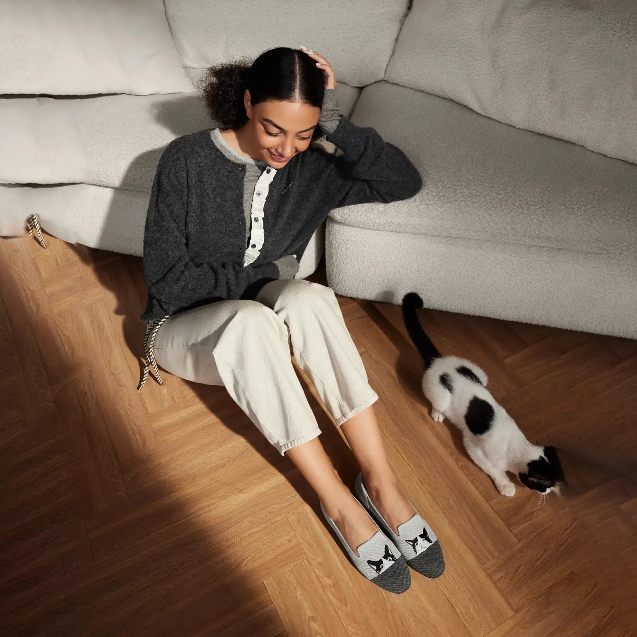 Pet mom sitting on parquet floor with her tuxedo cat, wearing Audrey moo-cat embroidered loafers