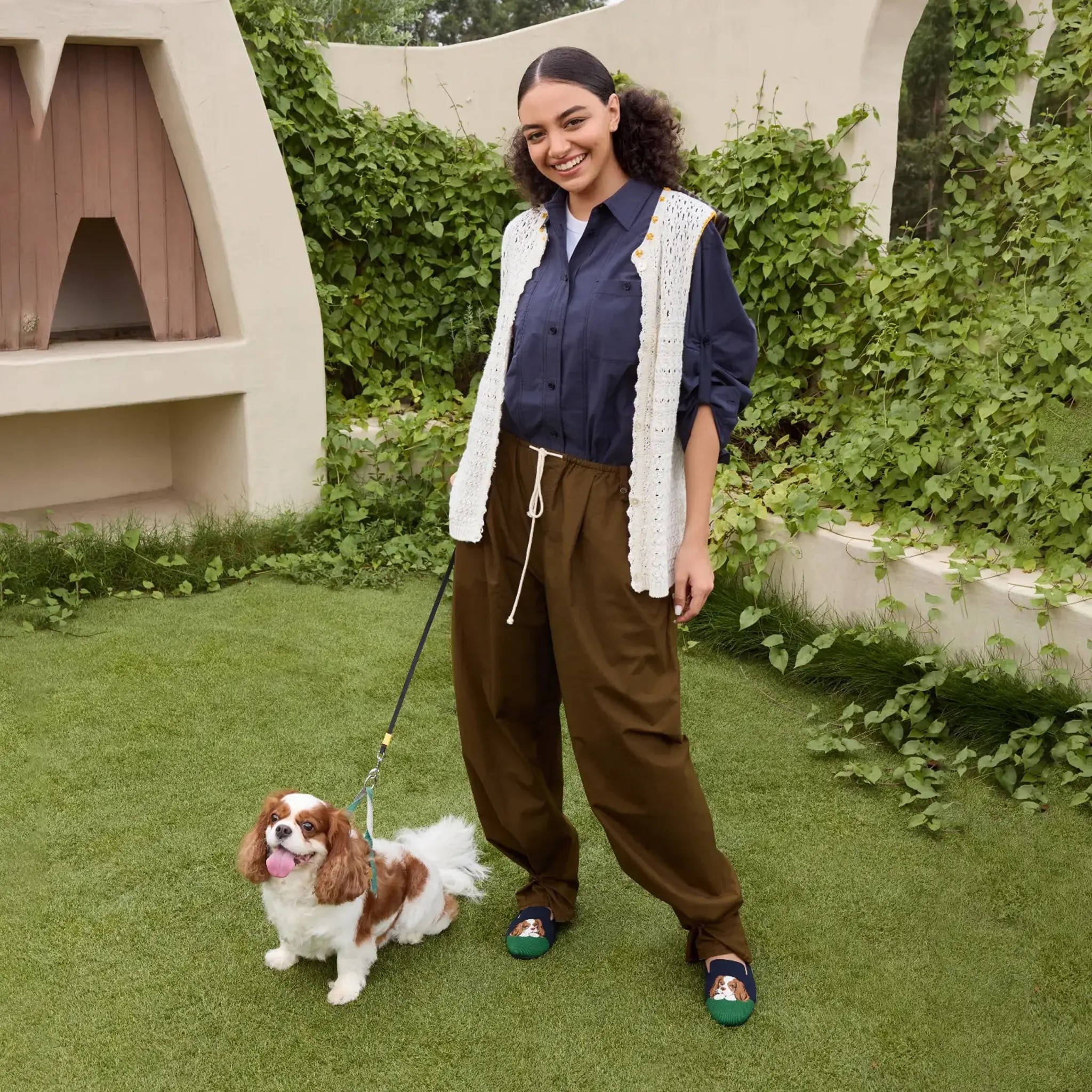 Smiling pet mom walking her Cavalier King Charles Spaniel in a garden, wearing Audrey cavalier embroidered loafers