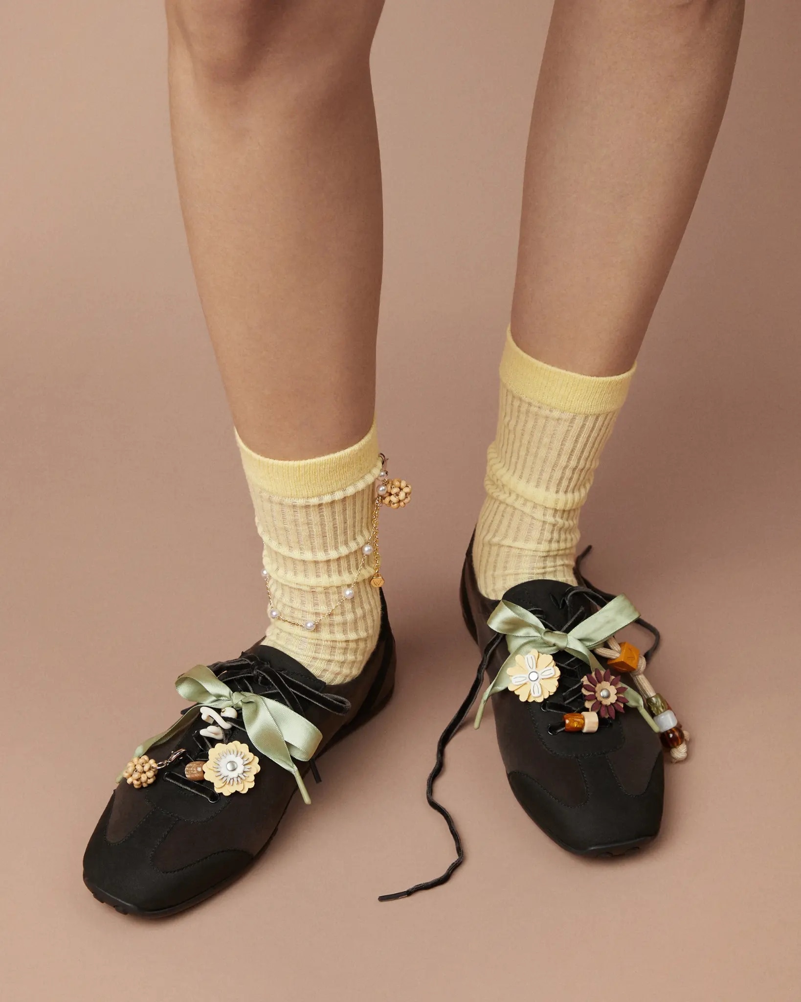 Model wearing black VIVAIA sneakers with yellow socks, sage ribbons and floral charms