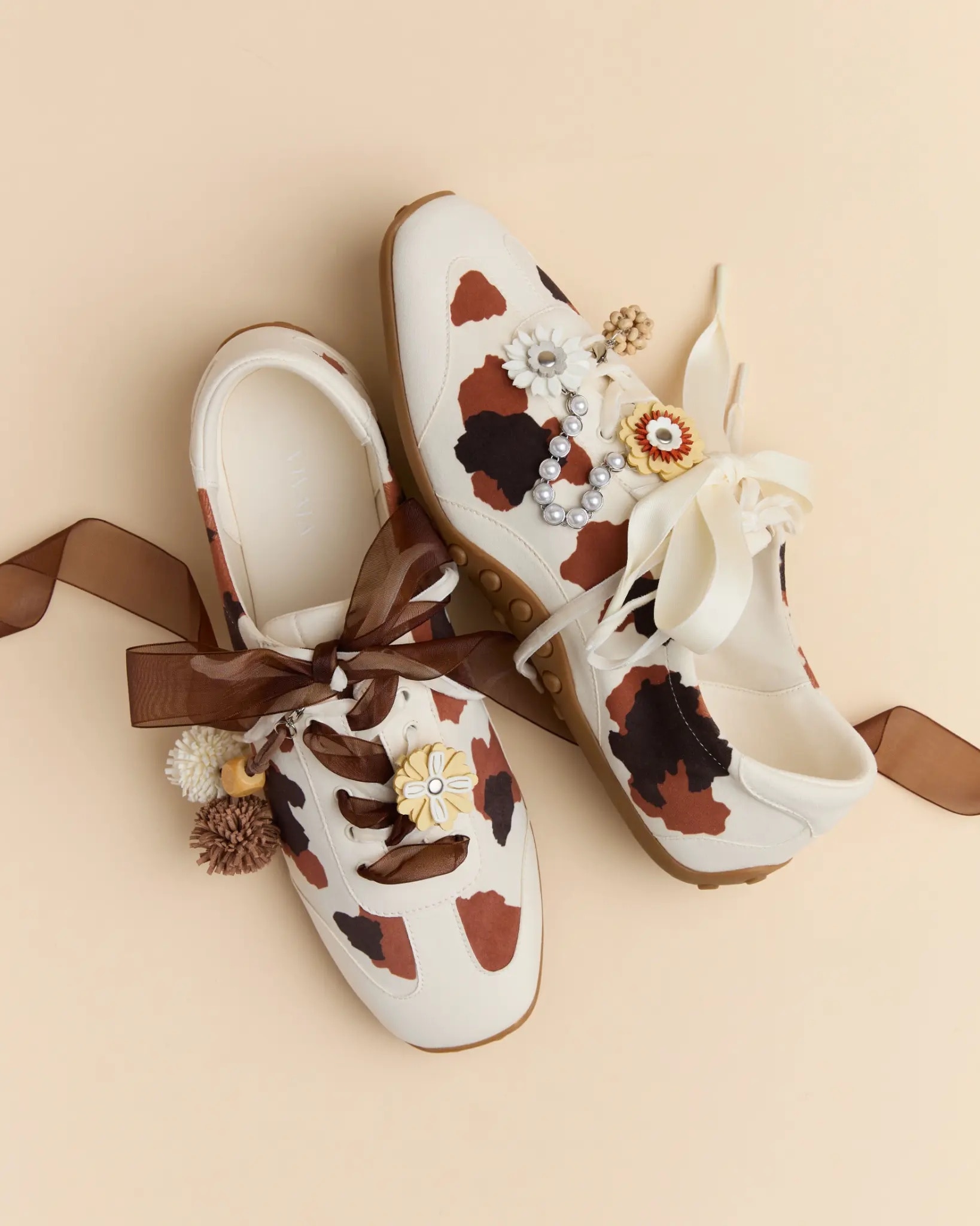 White cowhide VIVAIA sneakers styled with brown ribbons, flower charms and pearl details