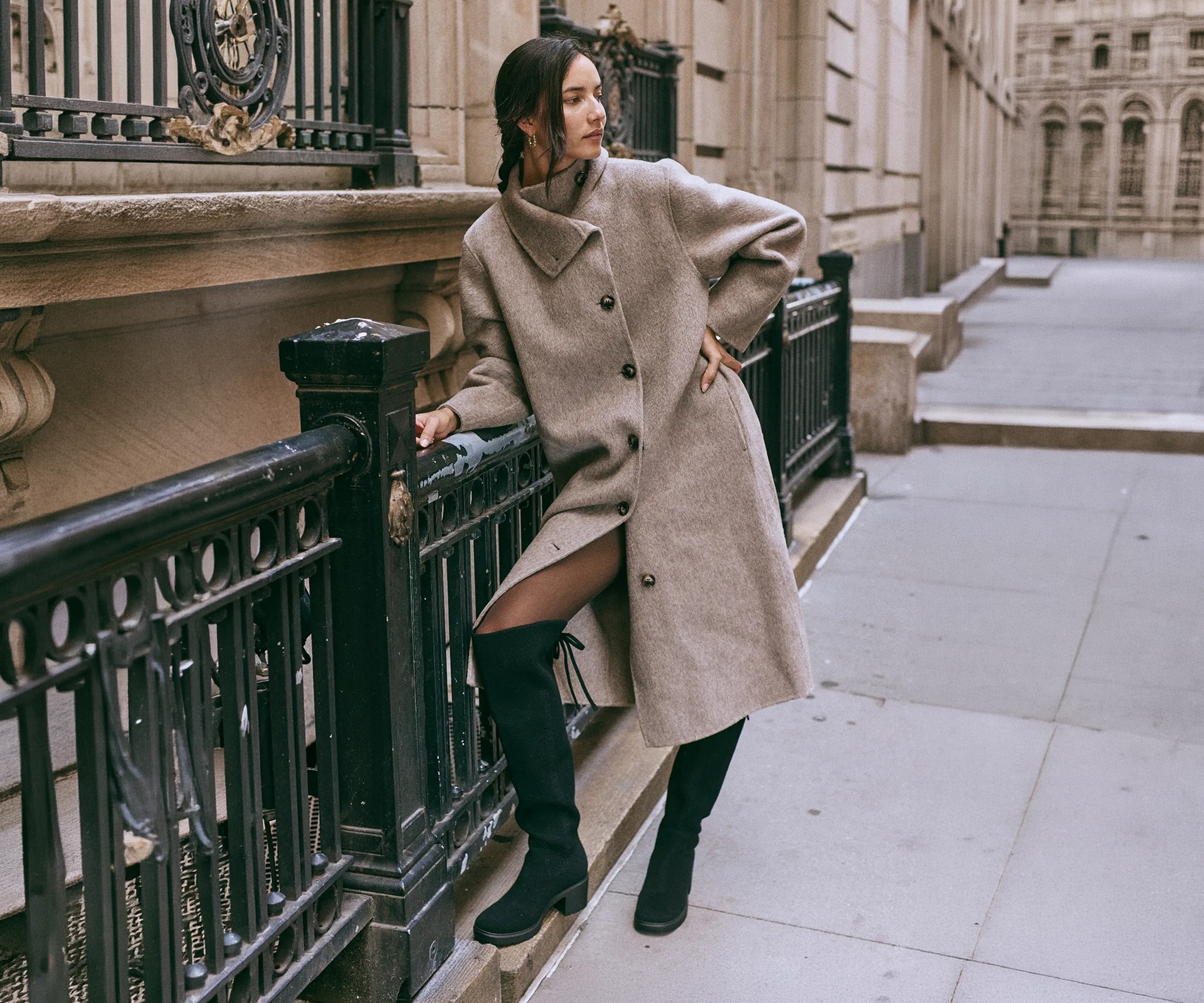 Gia 2.0 black boots styled with a taupe coat beside a city railing