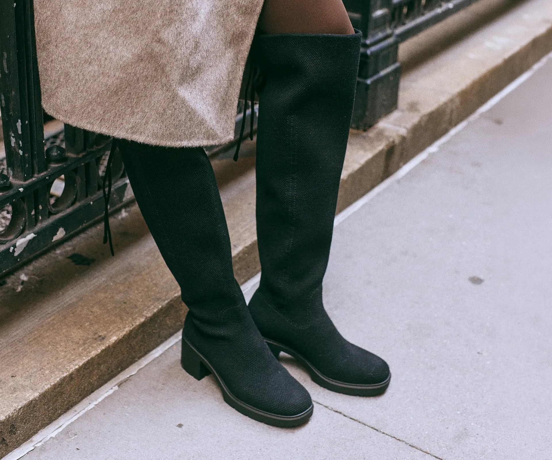Close-up of Gia 2.0 black boots styled with a taupe coat