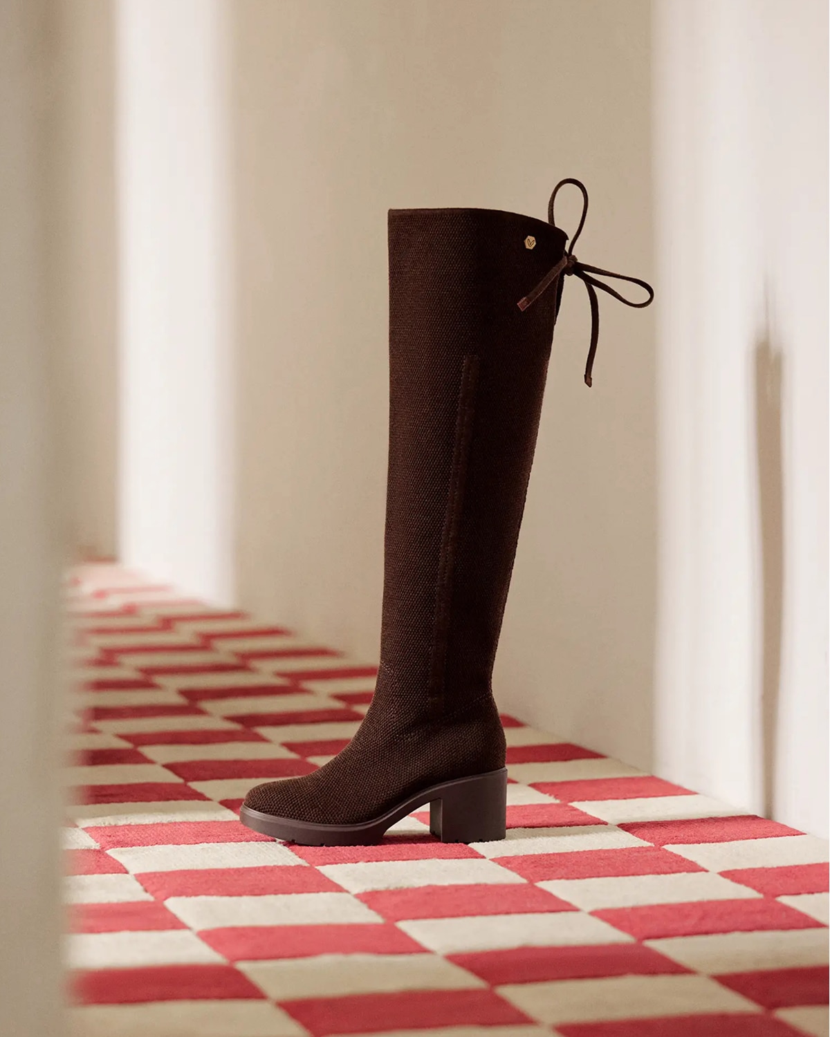 Chocolate knit knee-high boot with tie detail on a red and cream checkerboard floor