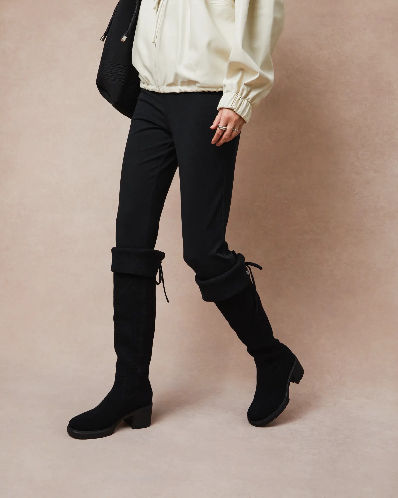 Black knit boots styled over black trousers with a cream blouse