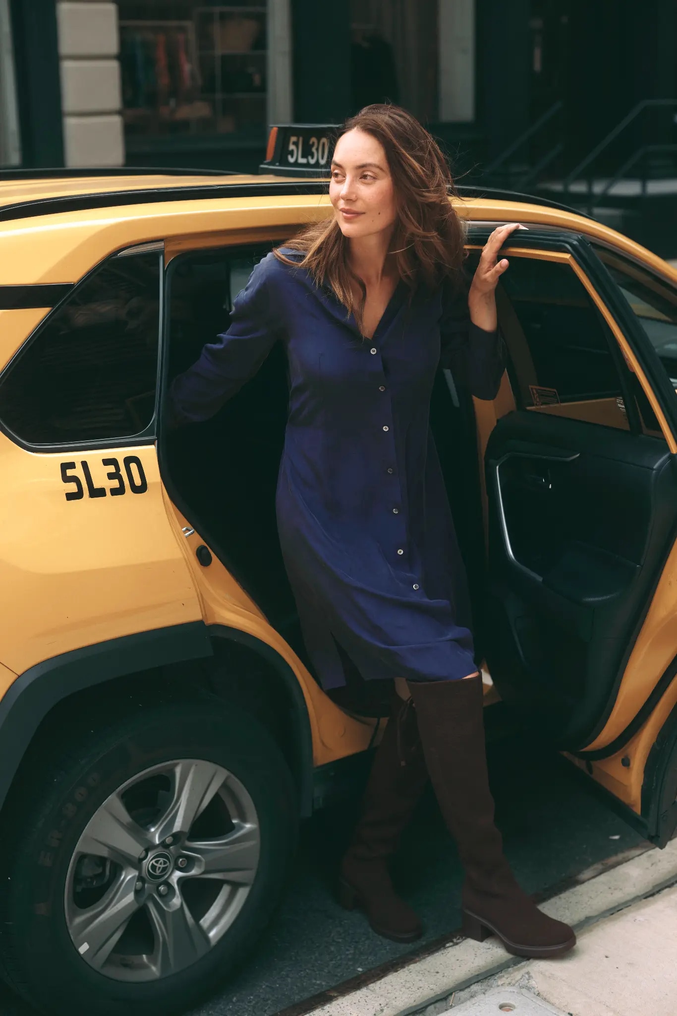 Navy shirt dress and chocolate knee-high boots beside a New York yellow taxi